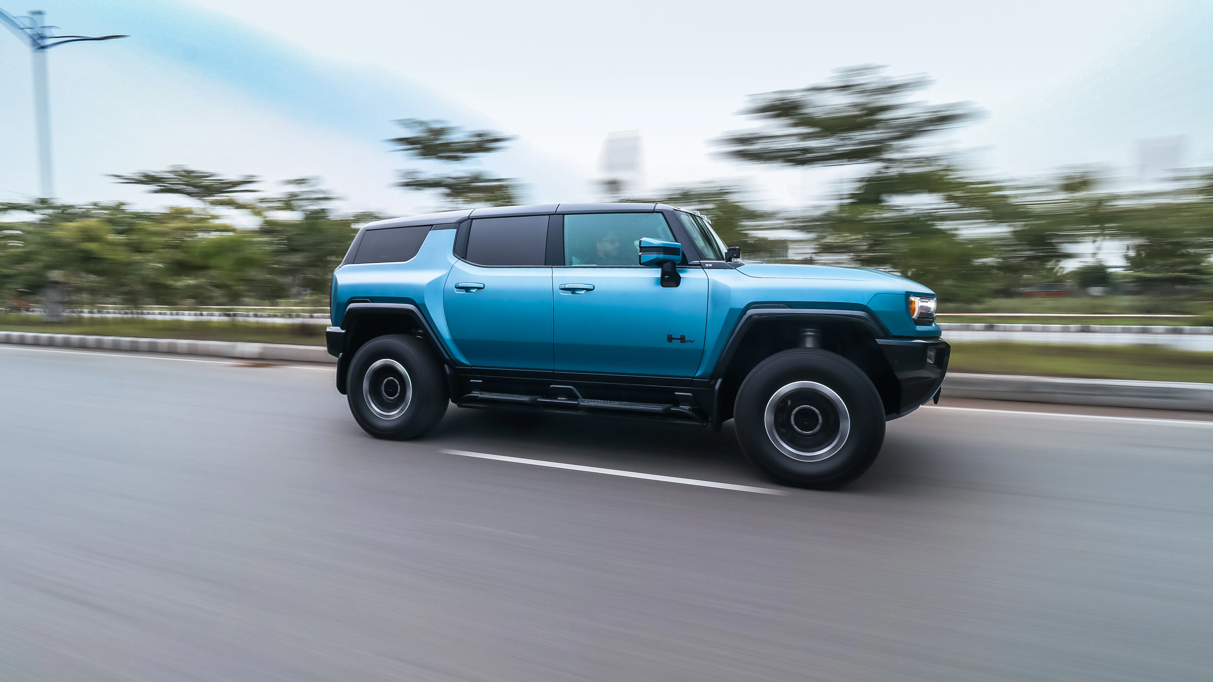 Side pan of the Hummer EV SUV at speed, trees blurred behind