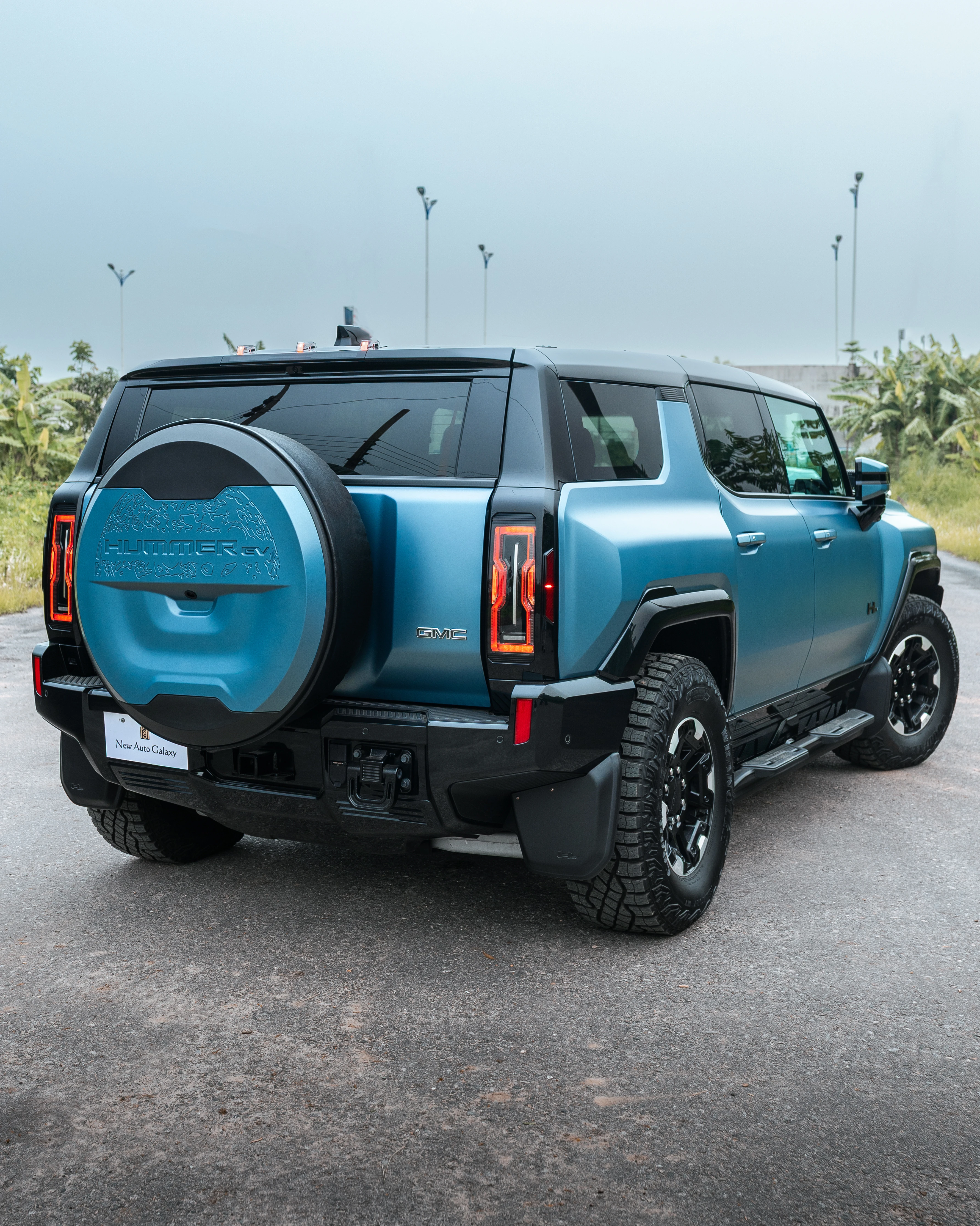 Rear three-quarter of the Hummer EV under a grey sky, lamp posts behind